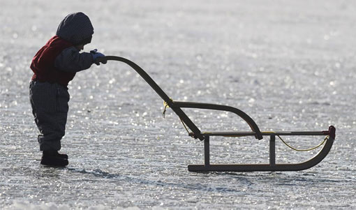 child pushing sled on frozen pond in Munich, Germany