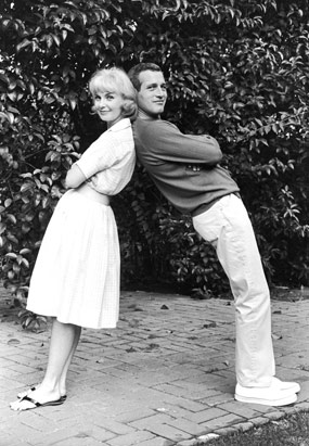 American actors Joanne Woodward and Paul Newman lean back to back on each other outdoors, in the early 1960s, a few years after they married