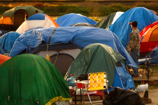 a homeless man looks out over tent city as the sun sets in Sacramento