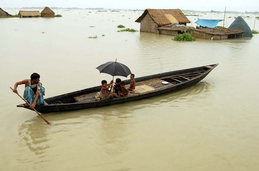 Flood crisis: A villager rows a boat past huts submerged in floodwaters in Bhakatpur, in the northern Indian state of Assam.